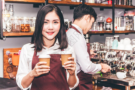 女小企业主在咖啡馆柜台酒吧后面微笑和拿着咖啡的肖像在咖啡馆使用咖啡机图片