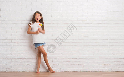 白砖墙上的西班牙裔小孩在家吃棒糖图片