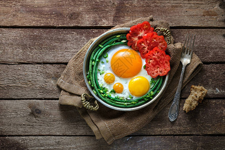太阳边煎鸡蛋在铜锅里配有西红柿和绿图片