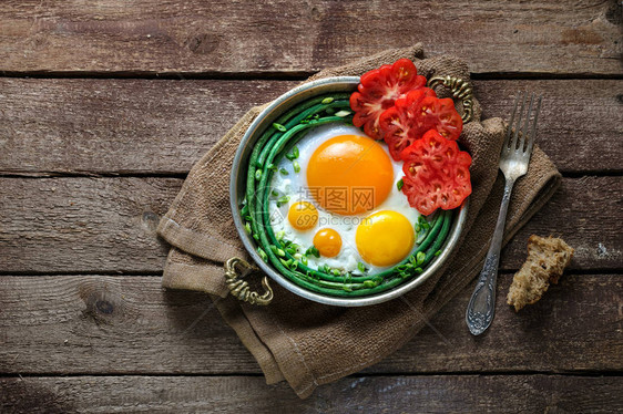 太阳边煎鸡蛋在铜锅里配有西红柿和绿图片