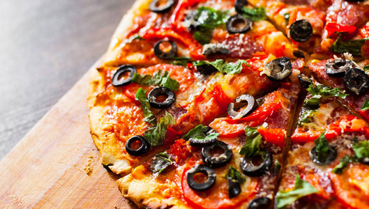 披萨片配马苏里拉奶酪意大利腊肠胡椒意大利辣香肠西红柿橄榄香料和新鲜罗勒木制背景上的图片