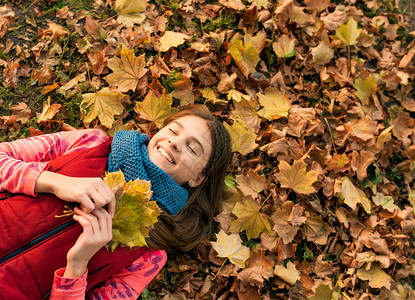 微笑着躺在秋天枫叶上的年轻女孩在户外秋天一个美丽微笑的少年的画像年轻的少女看着相机秋天图片