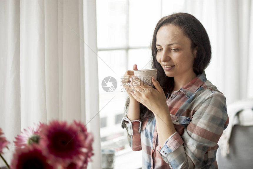快乐的女孩手里拿着一杯香浓的咖啡在家靠窗的客厅吃早餐不错文图片