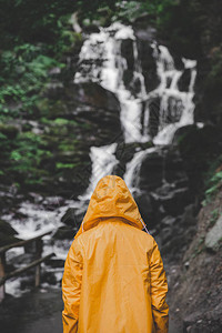 身穿黄色雨衣的人在看瀑布从后面查看图片