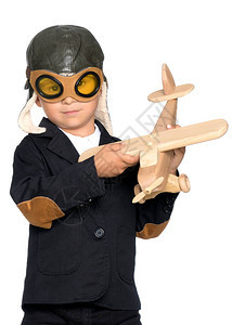飞行员头盔中的男孩正在玩具木制飞机他梦想成为一名飞行员快乐童年的概念图片