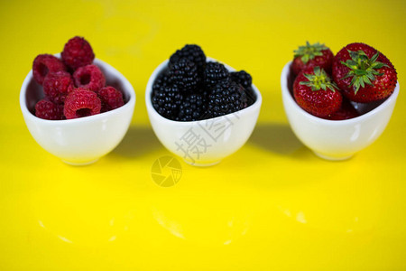 碗里的草莓黑莓和覆盆子黄色背景图片