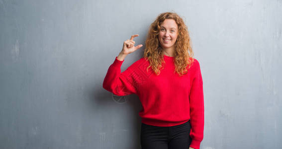 年轻的红发女人在灰色的垃圾墙上穿着红色毛衣图片