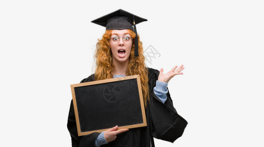 穿着毕业制服的年轻红发女学生拿着黑板非常高兴和奋图片