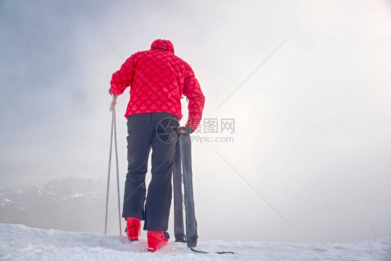 身着红黑整体短板滑雪手里拿着杆子的高大滑雪者站在白雪皑的深图片