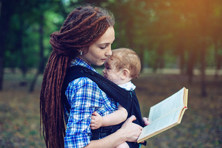 美丽的妈带着婴儿在人机工程学背包里在公园里读童话家庭生活图片