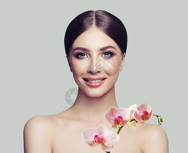 美丽的女人与健康的皮肤和白色背景上的粉红色兰花面部护理美容图片