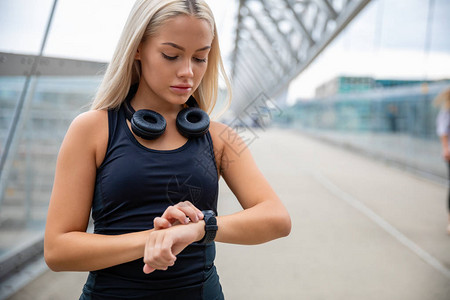 美丽的年轻女子在城市桥上健身后使用智能手表检查心跳率Smart图片