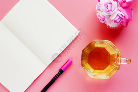 在粉红色背景上开着笔记本笔和花束的咖啡杯图片