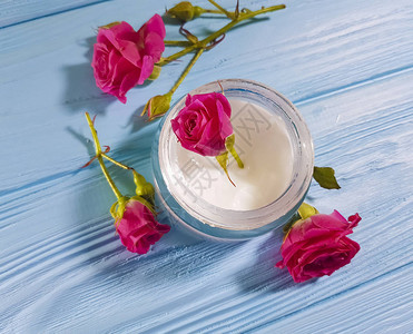 蓝色木质背景中的奶油色化妆品玫瑰花图片