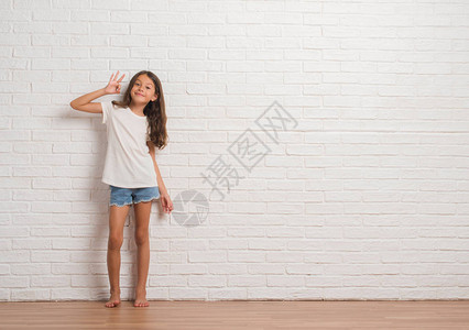 年轻的西班牙小孩在白砖墙上挥舞着正面的笑容图片