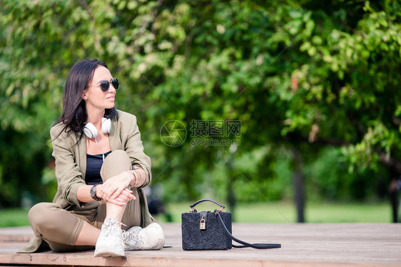 美丽的女人坐在公园里看手机上的短信白种人女孩正在听音乐并在智能手图片