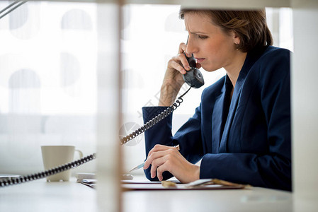 女商人或女经理在看文件时带着担心的表情在固定电话上交谈通过内部图片