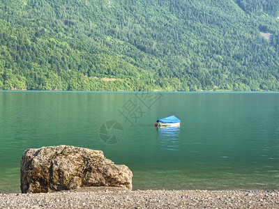 在阿尔卑斯湖绿色蓝水位的小船山湖的白色石质海岸森林山图片