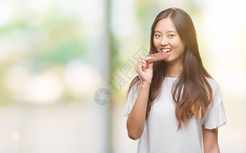 年轻的年青女在孤立的背景中吃巧克力棒自信地表现在聪明的面孔上图片