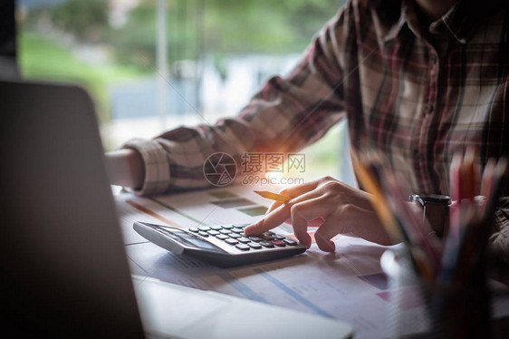 特写女商人使用计算器和笔记本电脑在办公室的木桌上做数学金融和商业工作背景税务会计统计和图片