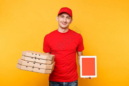 身穿红色帽子t恤的送货员在黄色背景的平板盒中提供食品订单披萨男员工比萨饼快递员持有带空白屏样机的平板电图片
