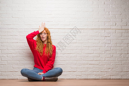 坐在砖墙旁的红发女青年对手头错误感到惊讶图片