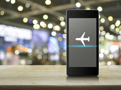 现代智能手机屏幕上的飞机平面图标在木桌上模糊光影购物中心图片