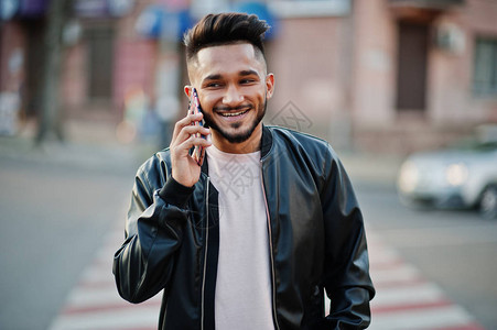 穿着黑色皮夹克的时尚印度胡子男在斑马线上行走印度模特在城市的街道上摆图片