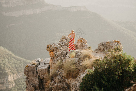 一位身穿红色和白色连衣裙的金发美女在悬崖顶上等待图片