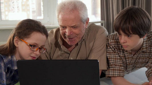 戴眼镜的小女孩帮助她的爷在笔记本电脑上打字高级灰人和他的两个孙子看着屏幕老年白人男对孙女说图片