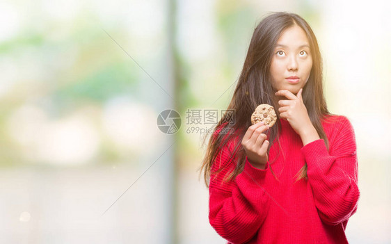 年轻的亚洲女在与世隔绝的背景下吃巧克力曲奇图片