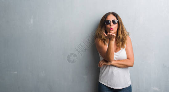 灰色墙壁上的中年西班牙裔妇女戴着墨镜看着镜头图片