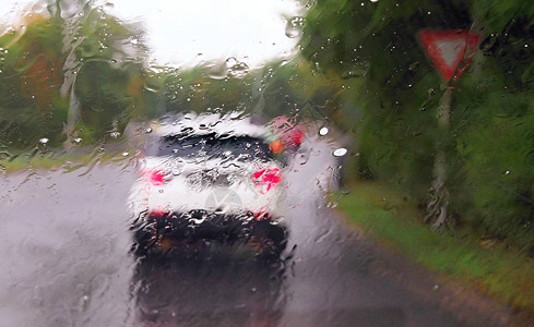 在交通繁忙的雨中驾驶汽车在驾驶汽车时通过带有雨滴的挡风玻璃图片