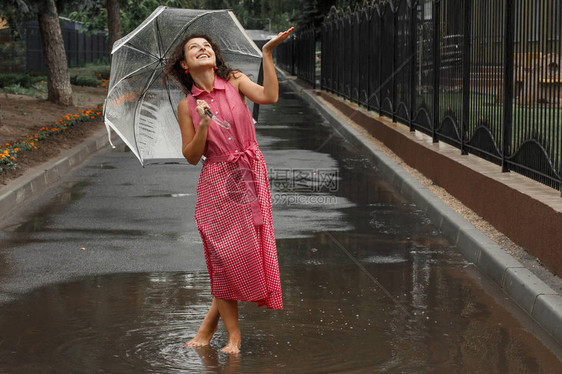 穿红裙子的年轻女孩穿着透明的伞子在雨中跳舞图片