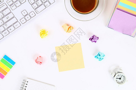 咖啡杯和键盘旁边的白色桌面上的彩色便签贴纸顶视背景图片