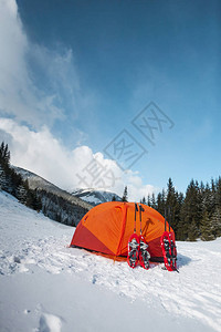 帐篷附近的雪鞋和登山杖在森林和山脉的背景下进行冬季远足的设备在山上露图片