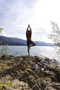 在湖边的岩石上练习瑜伽的人背景图片