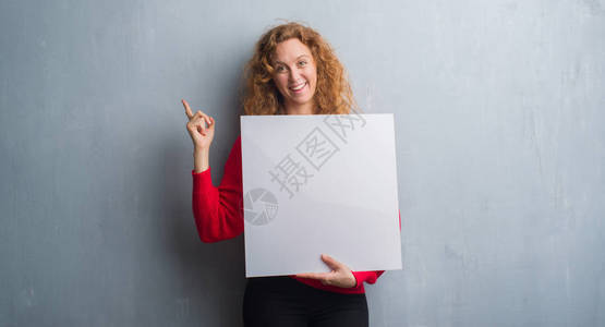 红发女青年在灰墙上挂着广告横幅的灰墙上图片
