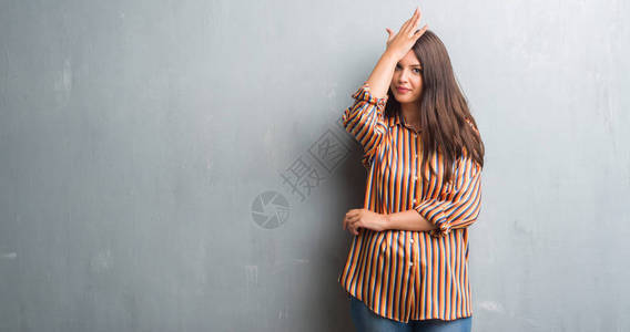灰色墙边的黑发年轻女人因犯错而惊异于手顶头部图片