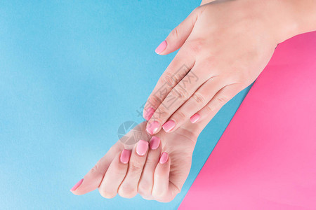 在美丽的蓝色和粉红色背景上涂有粉红色指甲油的女孩手图片
