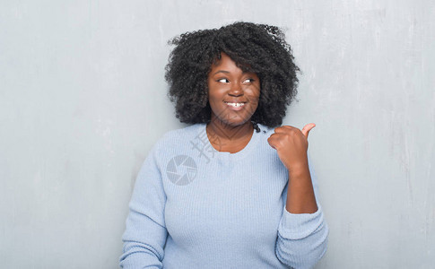 年轻的非洲裔美国女人在灰色的垃圾墙上穿着冬季毛衣图片