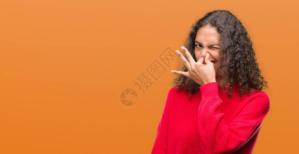 身穿红色毛衣的年轻西班牙裔妇女闻到某种臭味和恶心难以忍受的气味图片