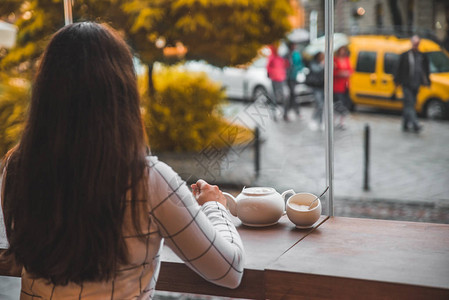 坐在咖啡馆里的女人带着大玻璃窗和美丽的秋天城市街道景图片