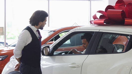成熟的男人在汽车经销店选择一辆新车专业的汽车经销商为他的客户打开汽车的门进入一辆新车的人销售图片