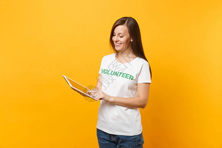 在白色t恤与书面题词绿色志愿者使用平板电脑孤立在黄色背景上的女人的肖像自愿无偿帮助背景图片