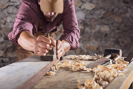 木匠在石墙前用手刨和其他木板将桌子上的长木梁弄平图片