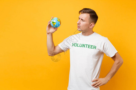 男人在白色t恤的肖像与书面题词绿色标题志愿者持有在棕榈世界孤立在黄色背景自愿无偿帮助背景图片