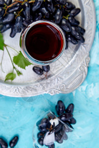 红酒概念与瓶子玻璃和葡萄在蓝色背景的银托盘上图片