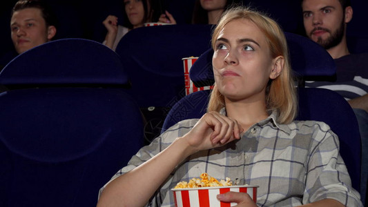 一个年轻漂亮的女人在当地电影院看电影时享受吃爆米花的短片有吸引力的女在电影院放松休图片