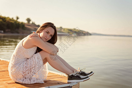 悲哀寂寞的年轻女人坐在码头上拥抱着膝盖图片
